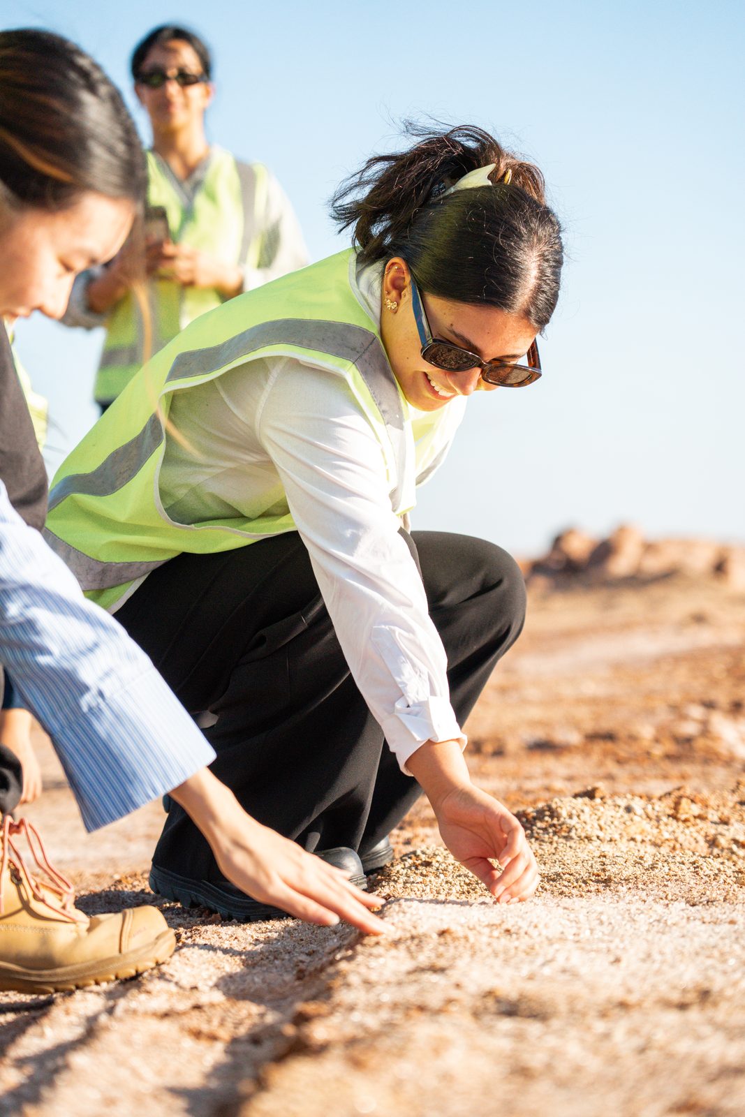 Taleena crouching in a hi-vis vest examining the ground with others during fieldwork